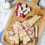 A few pieces pf colourful tarte flambée and some radishes on a cutting board