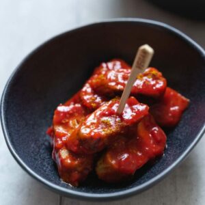 A serving of vegan currywurst with curry ketchup sauce adn curry powder for decoration.