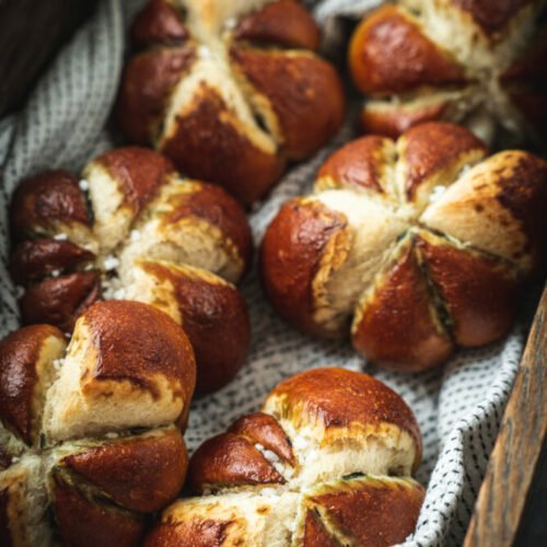 Six pieces of pumpkin shaped pretzel rolls on a napkin in a wooden box.