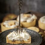 Apple tartlets with shortbread crust, cut in half on a small silver coloured plate. The apple tartlet is topped with vegan whipped cream.